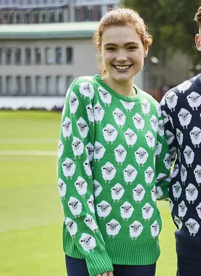 Smiling woman wearing green knit sweater with sheep pattern standing outside